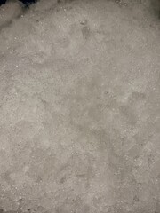 Close-up of crushed ice with sparkling texture, showing fine frozen crystals and a frosty surface under direct lighting.