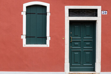 Green door and window with shutters on red wall in Burano Italy