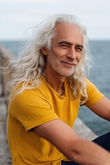 Fototapeta premium A man with white hair and a yellow shirt is sitting on a pier by the water. He has a smile on his face and he is enjoying the view