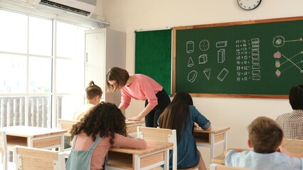 Smart teacher checking cute student homework while explaining idea at class. Attractive instructor...