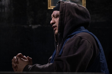 Side view of a praying man in a church, hands clasped, eyes closed, asking God for forgiveness, mercy, and love. Concept of divine help and hope in God.
