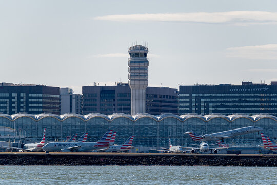 View of the air traffic control tower and terminal at Ronald Reagan Washington National Airport, with American Airlines jets parked at the gates and buildings of Crystal City in the background.