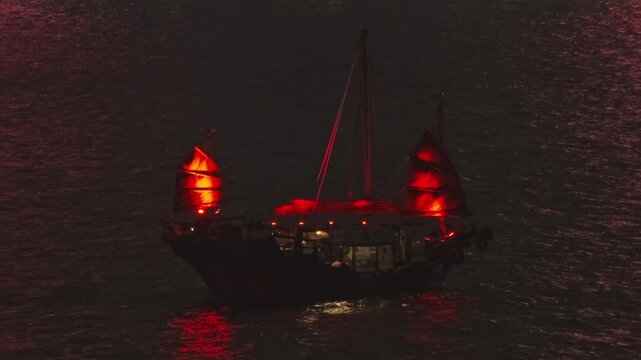 Traditional Chinese Junkboat with red sails sailing in Victoria Harbour at night, Hong Kong