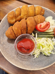 Čičinsko kepsnys, a special Lithuanian meat dish, is presented on a plate. The fried, golden-brown cutlets are served with a side salad of tomato, cucumber, and cabbage, plus ketchup. 
