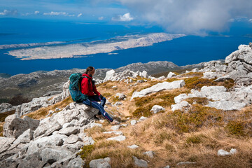 Young woman sitting on top of a mountain overlooking the sea. Croatia, Velebit mountain range