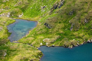 capra lake of fagaras ridge in summer. rippled blue water surface and green grass on the shore view from above. alpine pond carpathian mountains of romania. vacation in europe
