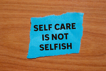 Self care is not selfish message written on ripped torn blue paper piece on wooden background....