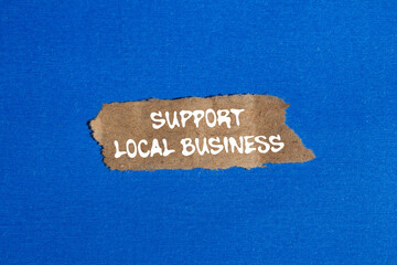 Support local business message written on ripped torn brown paper piece on blue background....