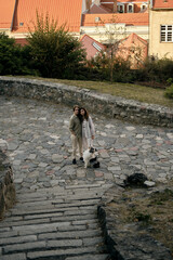 Young couple with a fluffy blue merle Australian shepherd dog standing on a stone square, colorful red rooftops of old town in the background. Peaceful outdoor moment in historical city.