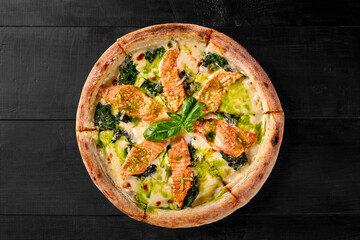 Delicious pizza with salmon, spinach and pesto on black wooden background