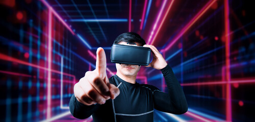 Professional male gamer with VR glasses pointing and playing game with glowing neon light. Excited...