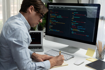 Fototapeta premium Stressful IT developer analyzing online software development information on pc and laptop with coding program on trial application project. Technical engineer writing crucial memo lists. Pecuniary.