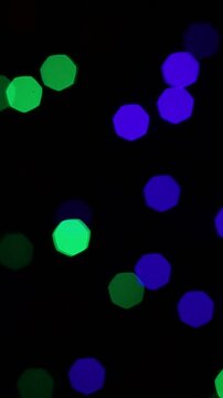 Una toma de cerca de varias luces de colores en forma de c&iacute;rculos en movimiento en la oscuridad. Desenfoque, efecto Bokeh. Video vertical