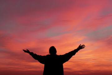 Fototapeta premium Silhouette of person with arms outstretched against vibrant sunset sky, conveying freedom, peace, and serenity