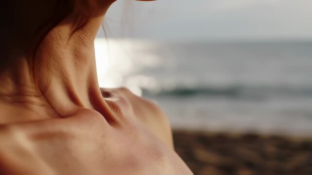 Close-up of beautiful woman's collarbones glistening in sunlight on a tropical beach with ocean backdrop