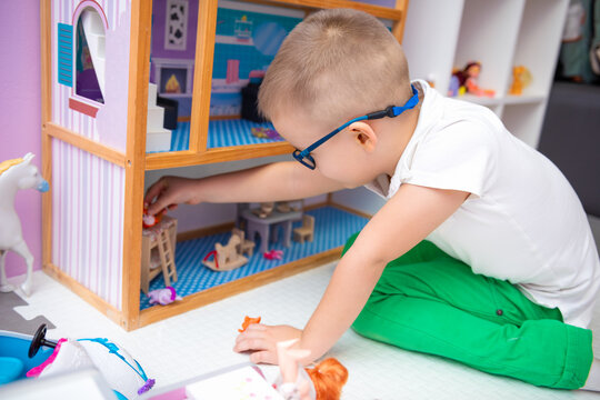 Boy is playing with a dollhouse. A dollhouse filled with furniture, dishes, dolls and animals.