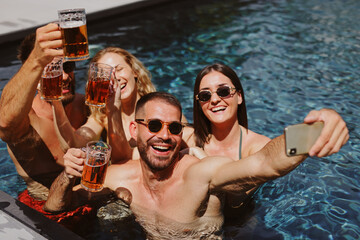 Group of friends enjoying a summer day taking a selfie while drinking beer in a swimming pool