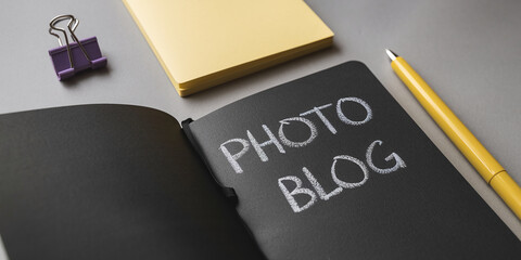 Open black notebook with "Photo Blog" written in chalk, alongside yellow pen and purple binder clip on gray surface Mockup for blog, website, or social media