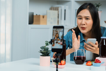 Smiling young beautiful Asian reviewing tasty mixed strawberry and cherry juice detox drinks,...