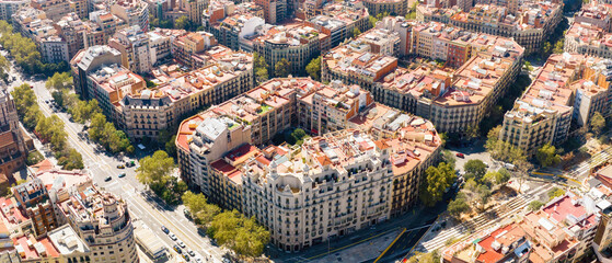 Obraz premium Aerial view of Barcelona's Eixample district with grid streets, green avenues, and historic buildings on a sunny day.