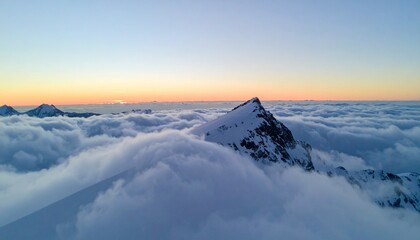Isolated snowy mountain peak piercing through dense sea of clouds during sunrise