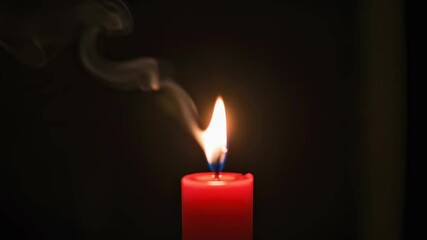 Red candle burning close up with smoke against black background. Slow rising white smoke stream from single red candle flame for solemn occasion or remembrance.