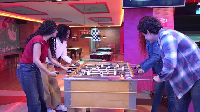 Friends experiencing high energy competition while playing foosball in vibrant bowling alley, capturing spirited interaction through slow motion dynamics