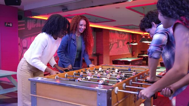 Group of friends enjoying a foosball game in slow motion at a bowling alley, celebrating a goal with high five