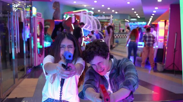 Young couple playing arcade shooting game, sharing joyful moment with smiling excitement and energetic interaction in colorful gaming environment