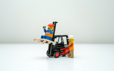 Obraz premium Tallinn, Harju, Estonia - 12.03.2023: Dangerous construction scene with LEGO workers, one sits unsafely on on a white background. One operates the forklift, the other sits smiling on a lifted pallet.