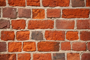Close-up view of a weathered red brick wall with rough texture and visible mortar lines, ideal as a...
