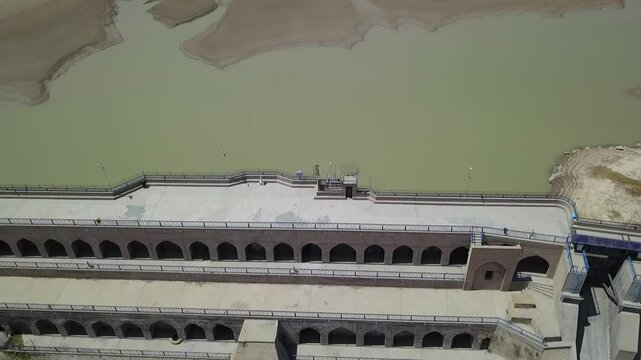 Drone shot directly above the dam capturing the greenish water in the upper reservoir and the cascading slope of the dam wall with multiple arched levels, offering contrast between nature and engineer