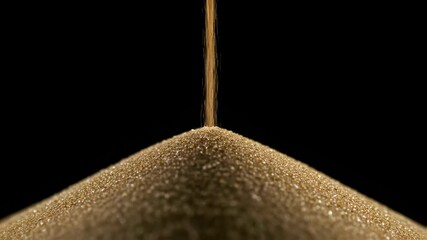 Golden sand pouring into heap on black background illustrating passage of time. Time passing in hourglass close up and slow video for concept of duration and countdown projects.