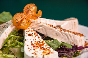 Lettuce salad with fresh cheese sprinkled with chili powder, bronze plate on a green background,...