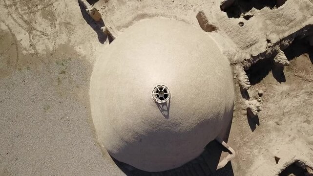 Drone pans across the front of a traditional Persian yakhchal structure in khorasan iran, showcasing its smooth conical exterior, small door, and thick adobe walls designed for storing ice