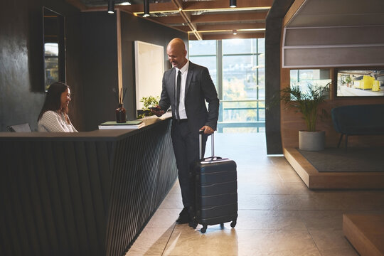 Travel, reception and mature man with luggage in hotel for business meeting, hospitality or check in. Service, concierge woman and person with suitcase for welcome, vacation or sales convention