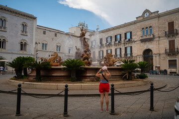 Woman in red shorts and no bra top, walking in street of Syracuse, Sicily. Rear view of happy girl in typical Italian old street. in Italy. Pretty fashion model. Travel and sightseeing journey concept