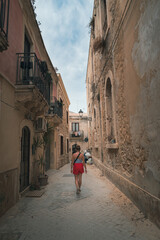 Woman in red shorts and no bra top, walking in street of Syracuse, Sicily. Rear view of happy girl in typical Italian old street. in Italy. Pretty fashion model. Travel and sightseeing journey concept