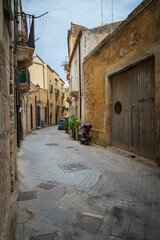 Narrow street in the old town of Syracuse in Sicily, Italy in a beautiful summer day. Travel and sightseeing journey concept. Motorbike parked beside the wall.