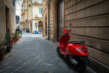 Narrow street in the old town of Syracuse in Sicily, Italy in a beautiful summer day. Travel and sightseeing journey concept. Motorbike parked beside the wall.