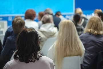 A group of people are sitting in a classroom, with a woman in the middle of the group wearing glasses.