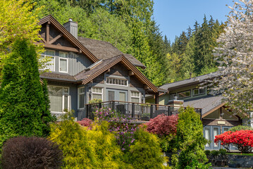 Top of grey stucco luxury house with shingle roof, green trees and nice windows in Spring in...