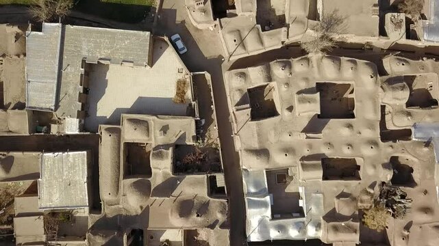 Detailed aerial view of a dense Persian desert village with closely packed adobe rooftops, domes, and windcatchers. The architectural composition reveals ancient Iranian urban design principles