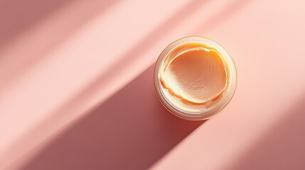 Open jar of beauty cream with a swatch on a pink peach background.