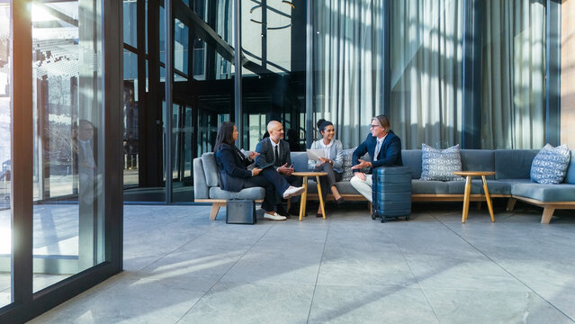 Travel, airport and business people on sofa, networking and international relations with meeting. Group, suitcase and employees on couch, luggage and first class lounge with conversation and luxury