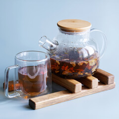 Glass teapot filled with fruit-infused tea atop a wooden stand, ideal for culinary blogs, product catalogs, and lifestyle presentations. Photo