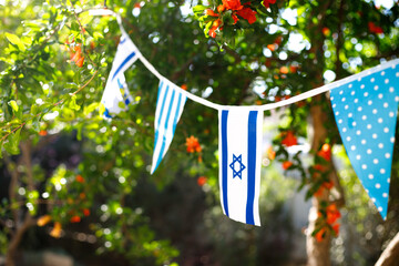 A garland of Israeli flags, among branches of a blooming pomegranate. Israel Independence Day - Yom Ha'atzmaut concept.