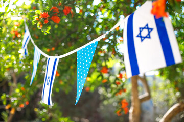 A garland of Israeli flags, among branches of a blooming pomegranate. Israel Independence Day - Yom Ha'atzmaut concept.