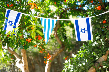 A garland of Israeli flags, among branches of a blooming pomegranate. Israel Independence Day - Yom Ha'atzmaut concept.