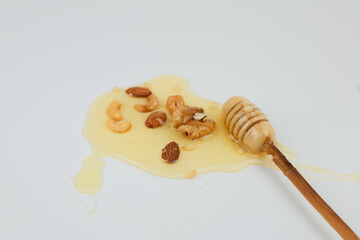 honey dripping from a spoonA mix of nuts lies in a puddle of liquid yellow honey, next to it lies a wooden spoon on a white background in close-up. The concept of a healthy snack, a natural dessert